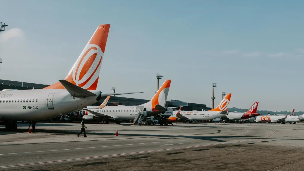 Multiple airplanes parked at an airport, with a focus on their tail fins featuring an orange design